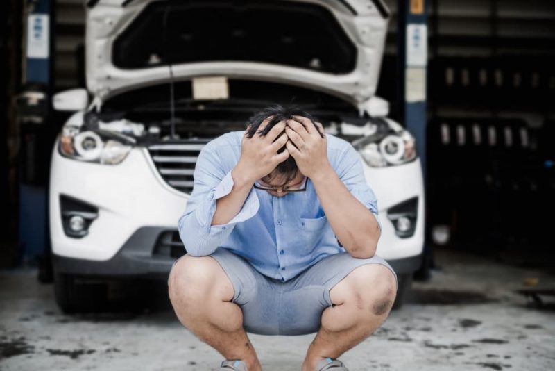 Distressed man sitting in front of car with open bonnet