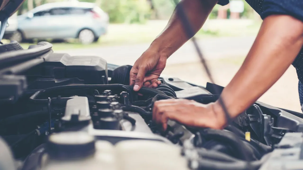 Hands working on an engine with the hood raised outdoors