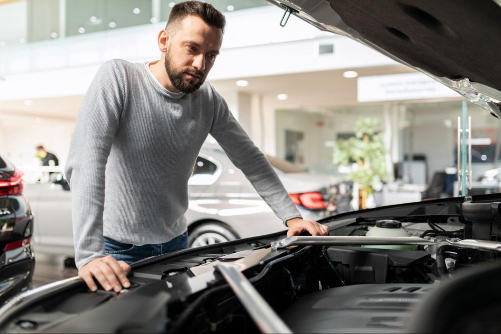 Man inspecting car engine in service center, representing concerns about PCM car replacement cost and vehicle diagnostics.