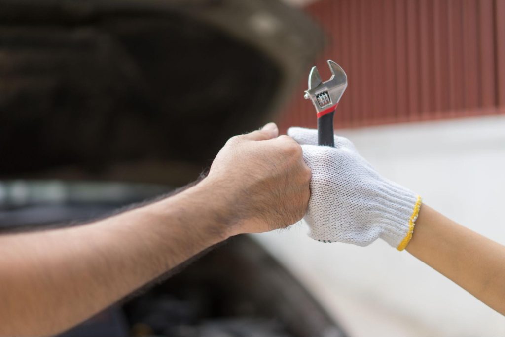 Mechanic handing over a wrench in front of a vehicle during PCM repair, symbolizing teamwork in locating where the PCM is located
