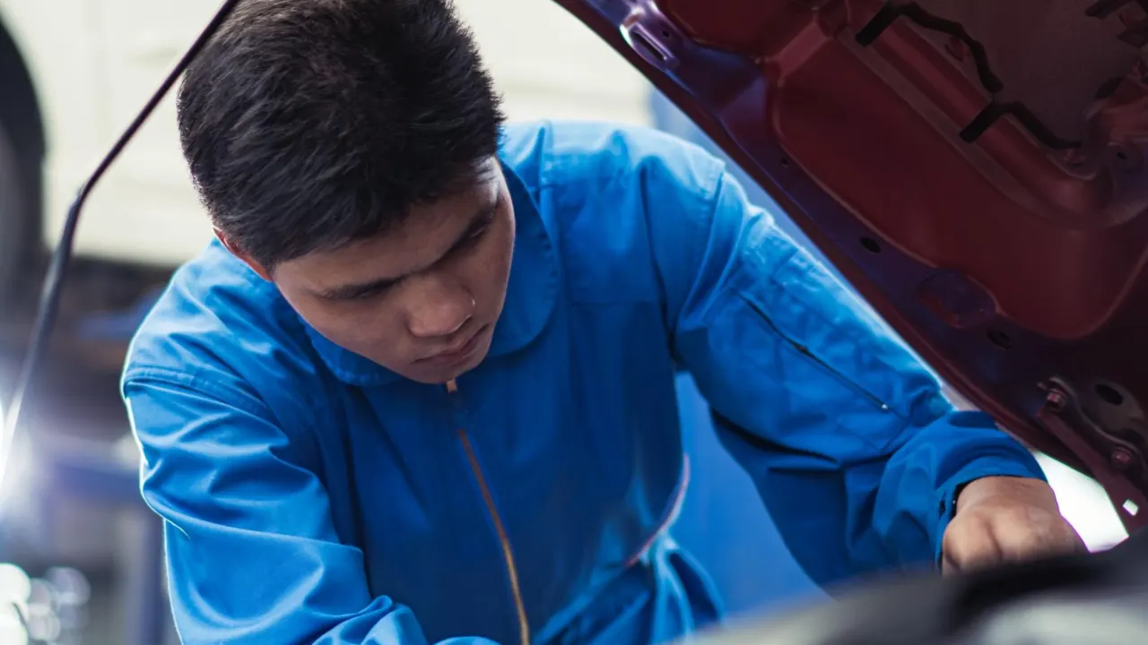 Auto technician in blue uniform checking under the hood to determine where the PCM is located in the engine bay