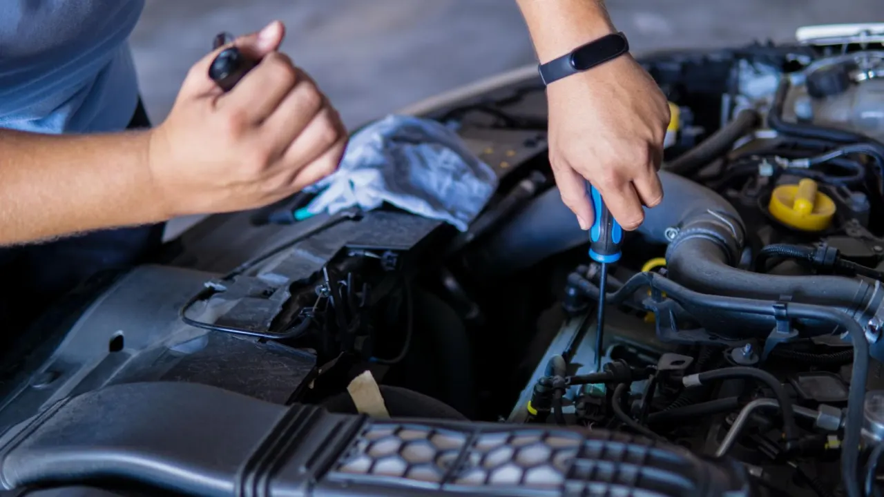 Technician using tools to perform engine computer module replacement under the hood of a car